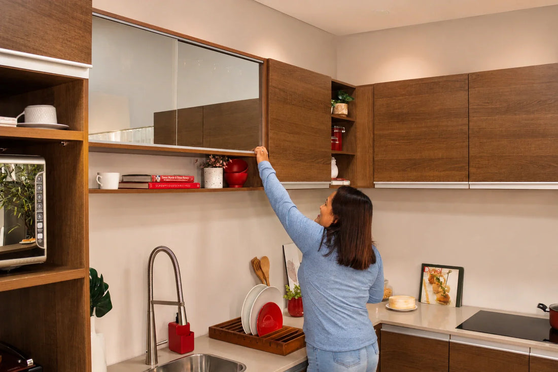Mujer abriendo gabinetes altos de madera línea Glamy de Madesa que aprovechan el espacio vertical en una cocina pequeña.